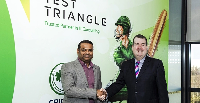 Two men in business suits shake hands in front of a green Test Triangle banner, signaling a IT consulting partnership or agreement.